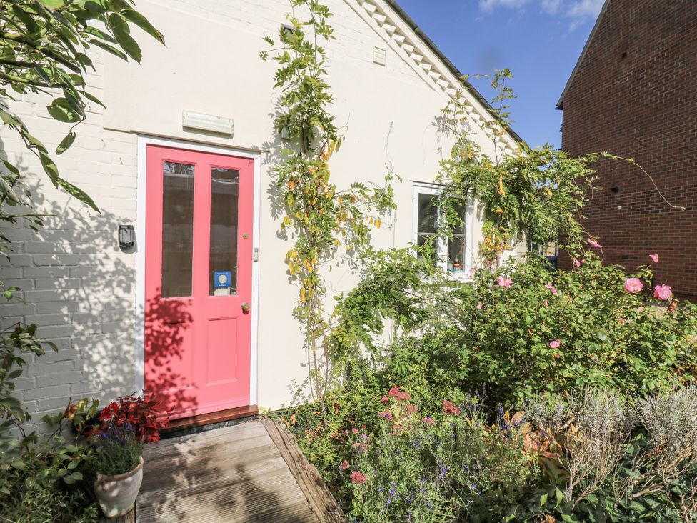 A front entrance with a pink door and flower bed at Over Village Studio in Over