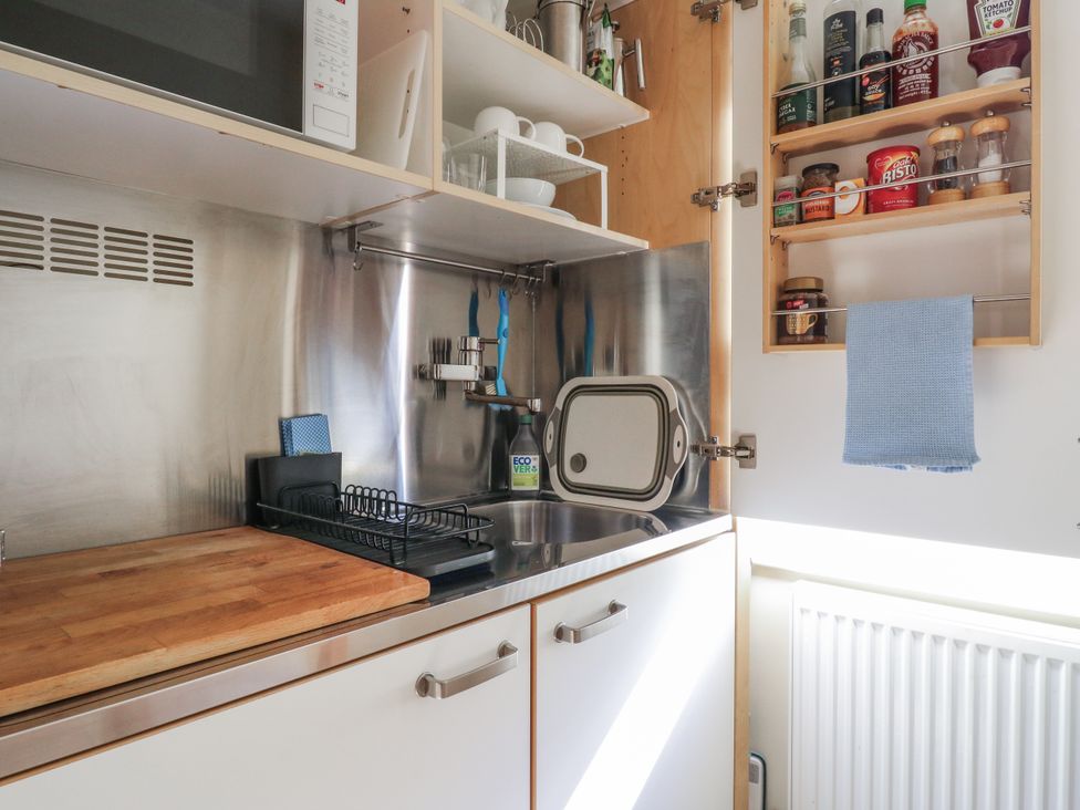 A kitchen with a sink, cutting board, and shelves containing spices and kitchenware at Over Village Studio in Over
