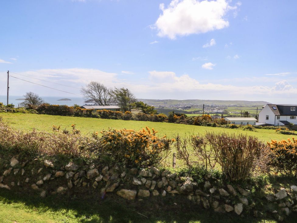 A view of grass and sea with houses in the background at Pen Y Garth in Mynytho near Llanbedrog