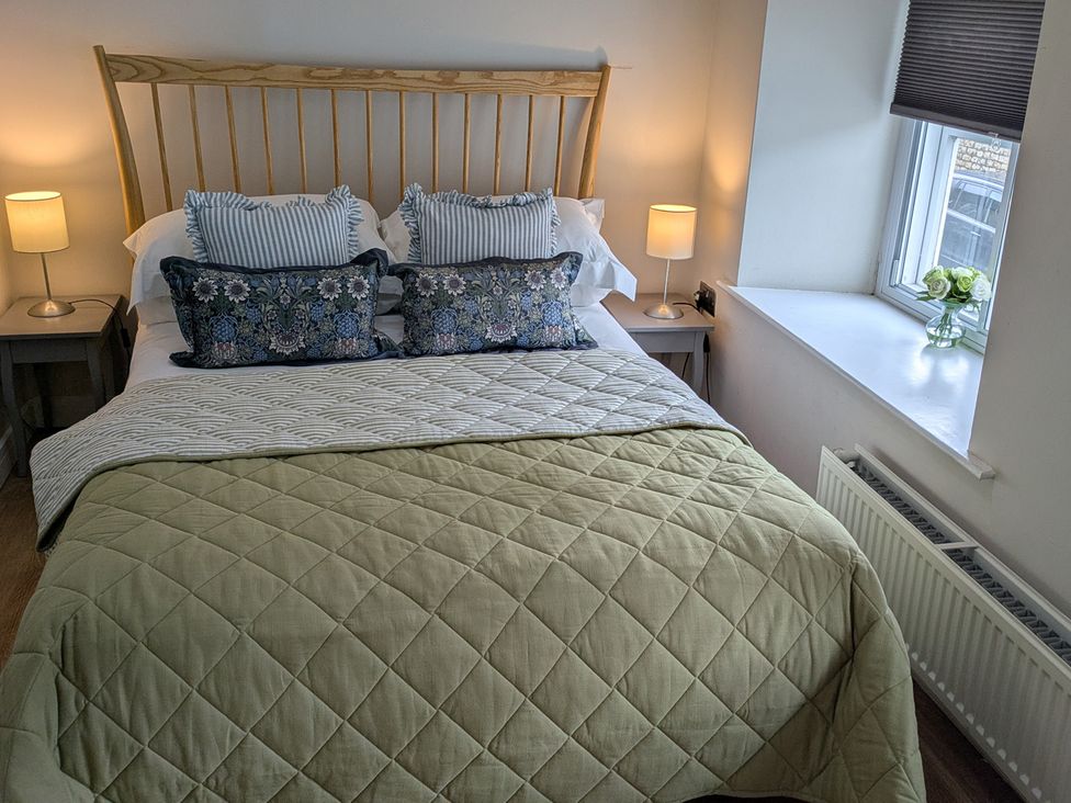 A bedroom with a bed, lamp, and flowers at Troopers Cottage in Frome