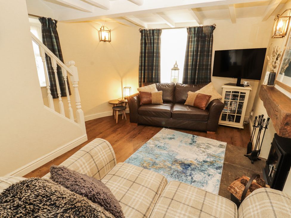 A living room with a sofa, television, and fireplace at Corner Cottage in Ingleton