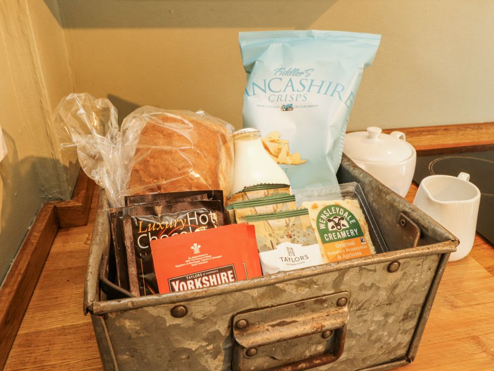 A basket containing bread, crisps, milk, hot chocolate, tea, and cheese at Corner Cottage Ingleton