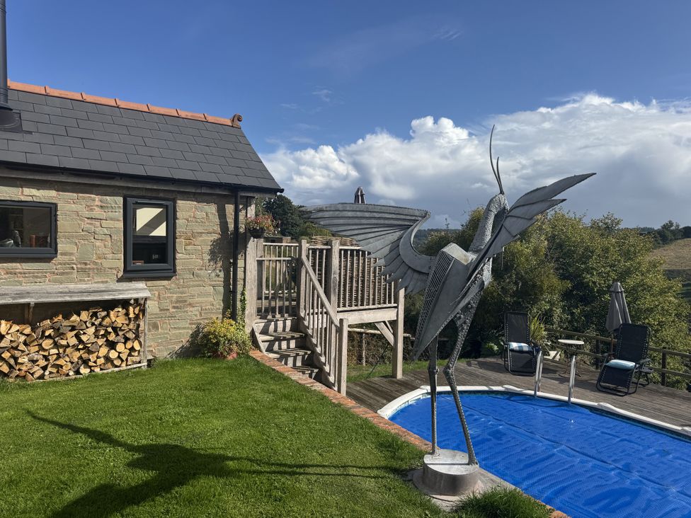 A house with a wooden deck, metal sculpture, and a pool at The Hideout in Llangrove