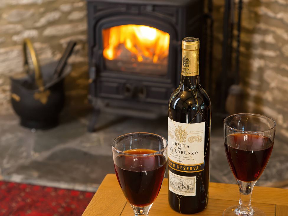 A wine bottle and two glasses on a table with a fireplace in the background at The Coach House in Kingston