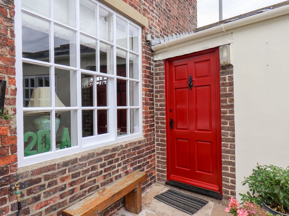 An outdoor area with a red front door and a bench at 20A St Hilda's in Whitby