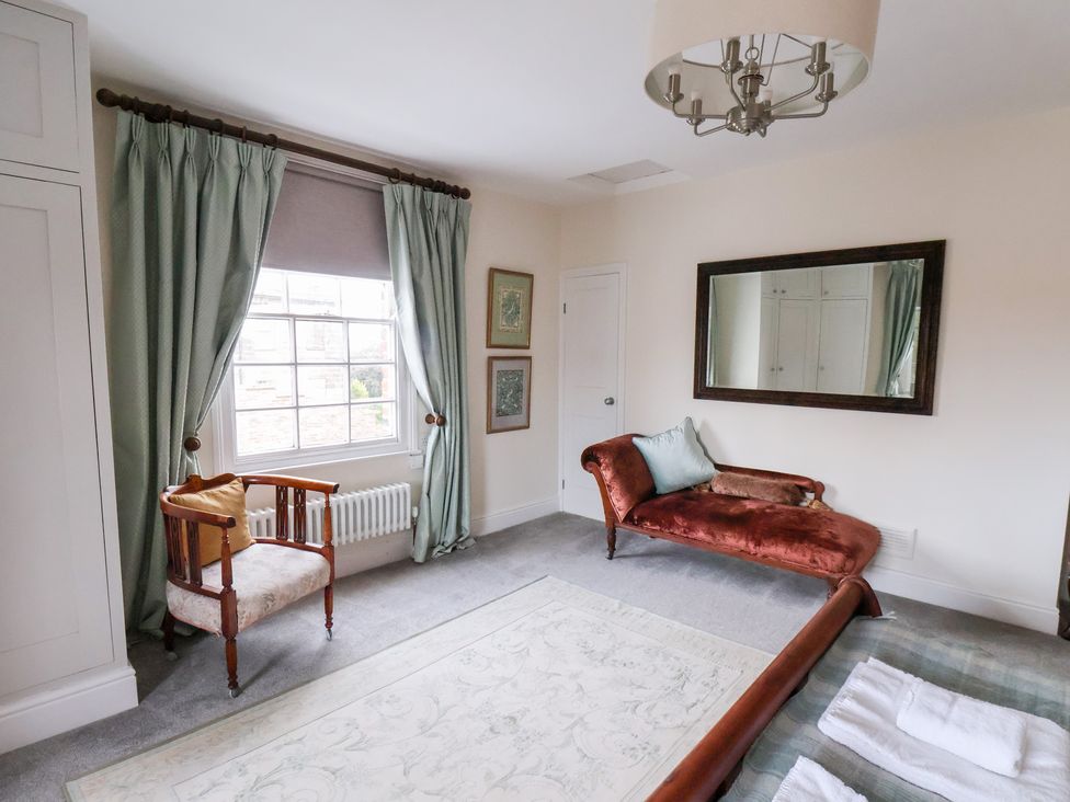 A bedroom with a window, curtains, chair, sofa, and mirror at 20A St Hilda's in Whitby