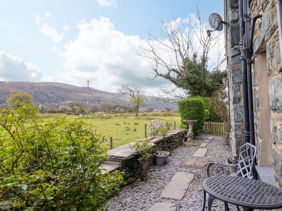 A garden area with stone wall, table, chairs and plants at Glyn Morfa in Harlech