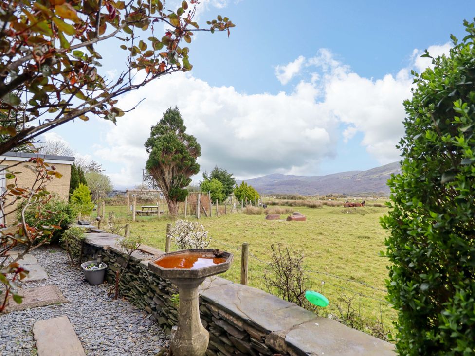 A garden view with a birdbath and trees at Glyn Morfa in Harlech
