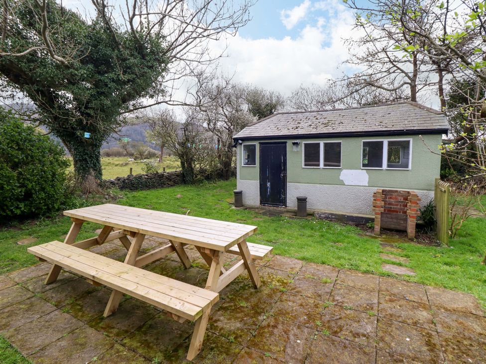 An outdoor area with a table and benches near a shed at Glyn Morfa in Harlech