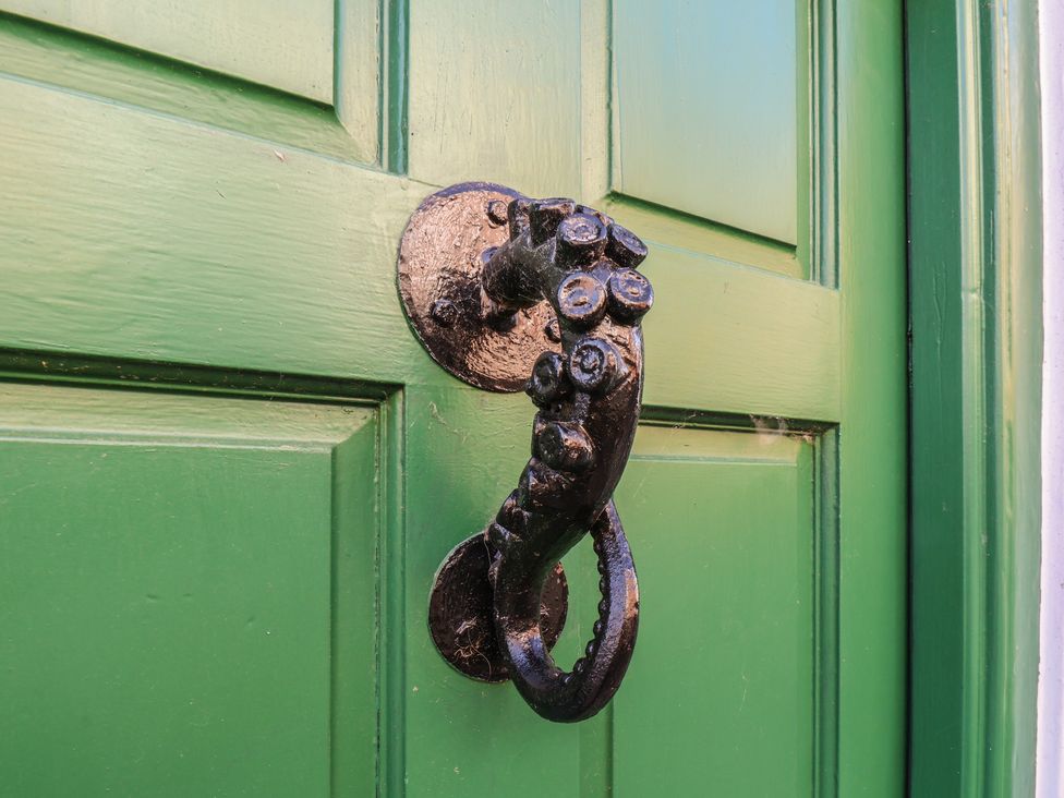 A green door with a decorative metal knocker at Cobbles House, Whitby