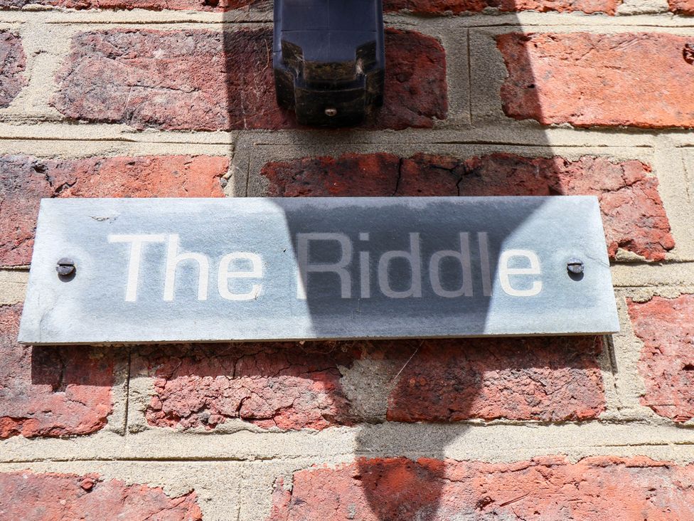 A metal sign with the text The Riddle mounted on a brick wall at The Riddle in Whitby