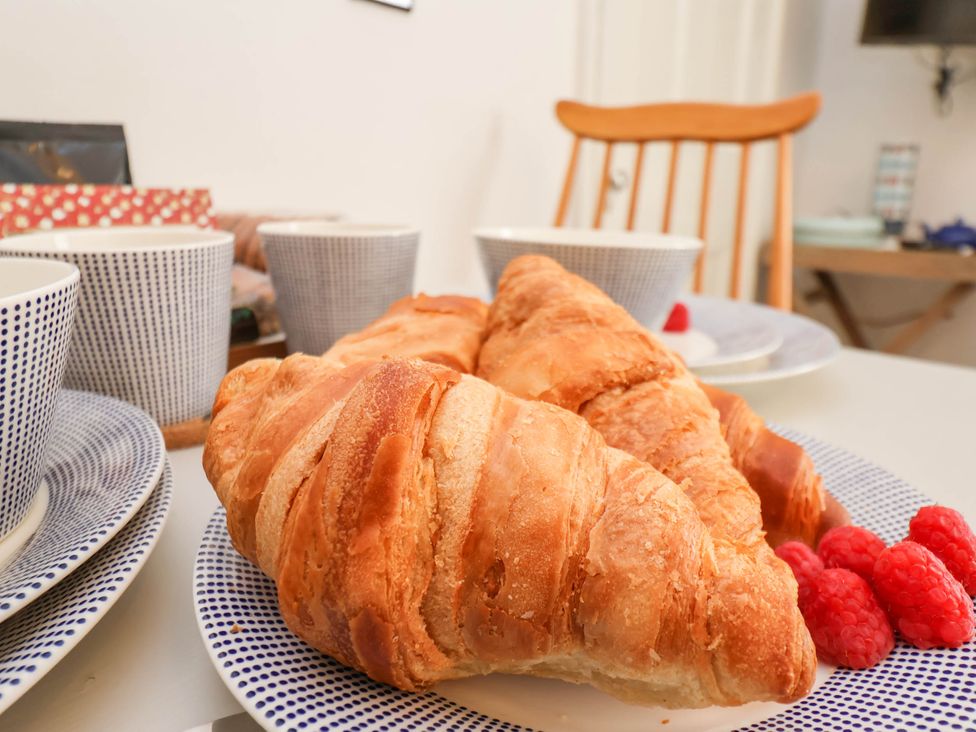 A table setting with croissants, raspberries, cups, and plates with a wooden chair in the background at The Riddle in Whitby