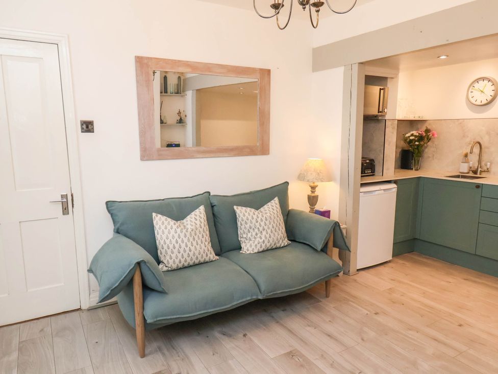 A small living area with a green sofa and two cushions beside a kitchen with green cabinets and a white fridge at The Riddle in Whitby