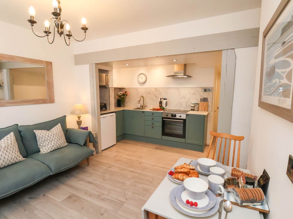 A kitchen and dining area with green cabinets a sofa and a table set with plates cups and pastries at The Riddle in Whitby