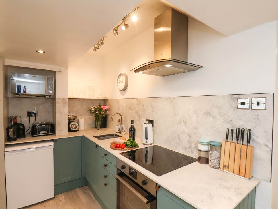 A kitchen with green cabinets a white countertop a microwave toaster kettle stove and a knife block at The Riddle in Whitby
