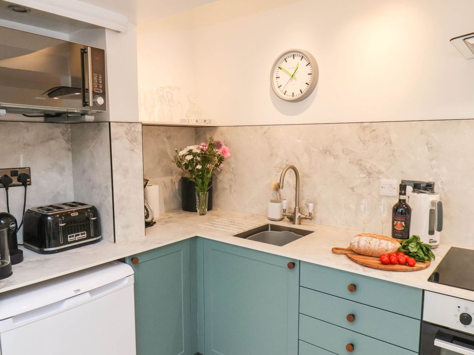 A kitchen with green cabinets a microwave a toaster a sink a cutting board with bread cherry tomatoes basil and a wine bottle at The Riddle in Whitby