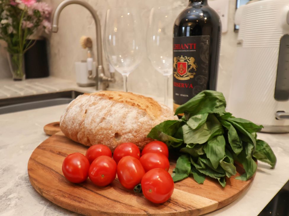 A kitchen countertop with bread cherry tomatoes basil wine bottle and two wine glasses at The Riddle in Whitby