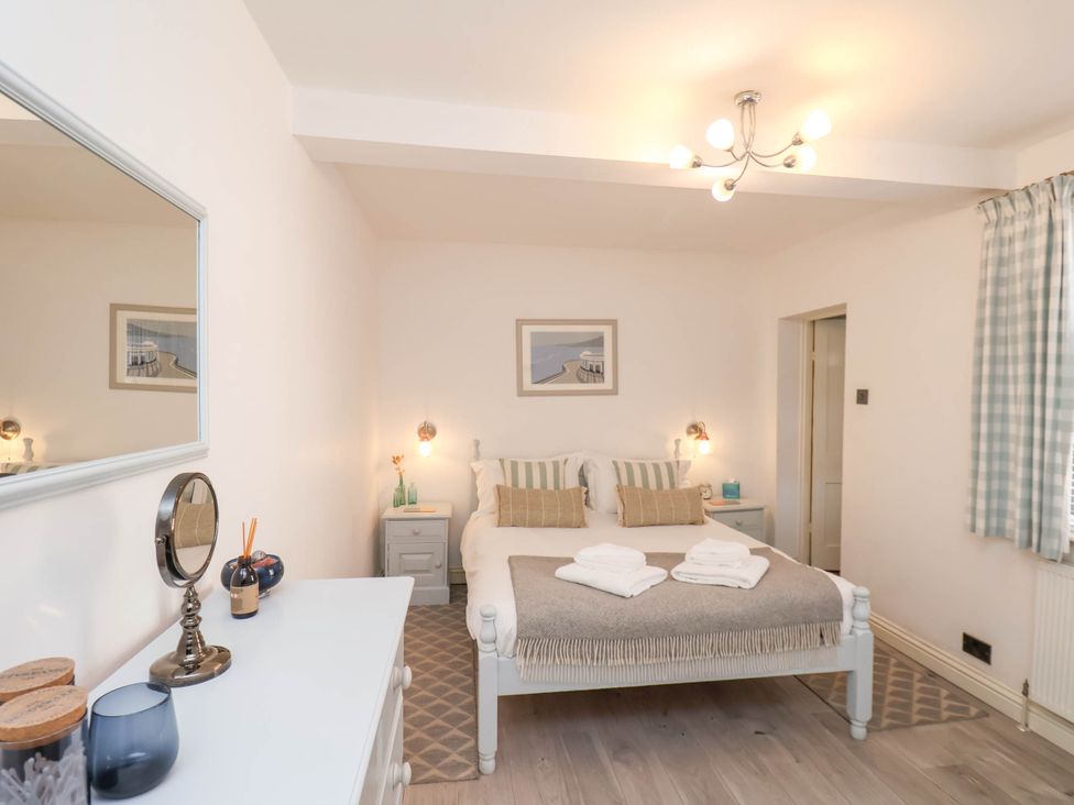 A bedroom with a double bed with pillows and folded towels bedside tables and a dresser with mirror at The Riddle in Whitby
