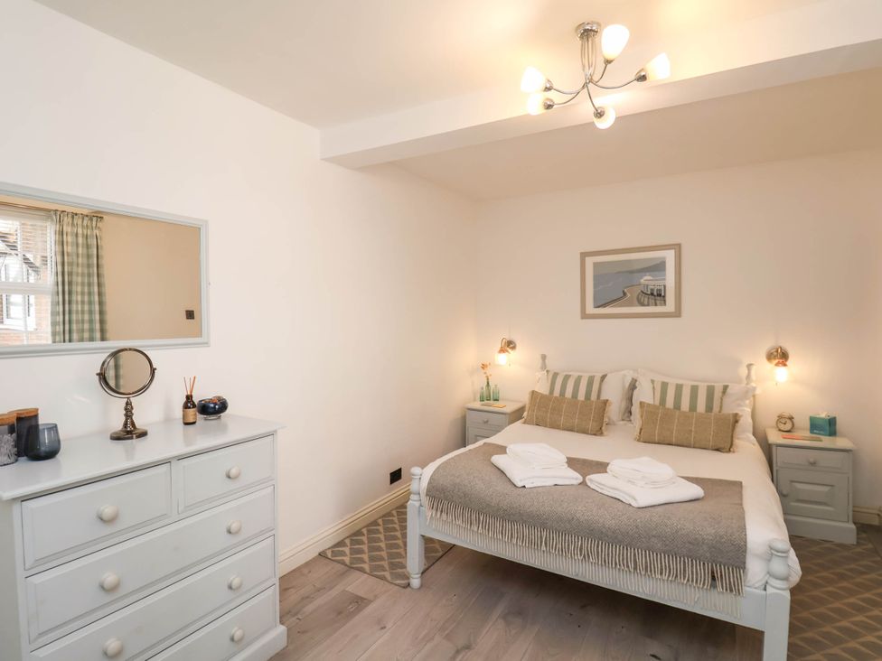 A bedroom with a double bed, two bedside tables, a dresser with a mirror, and wall art at The Riddle in Whitby