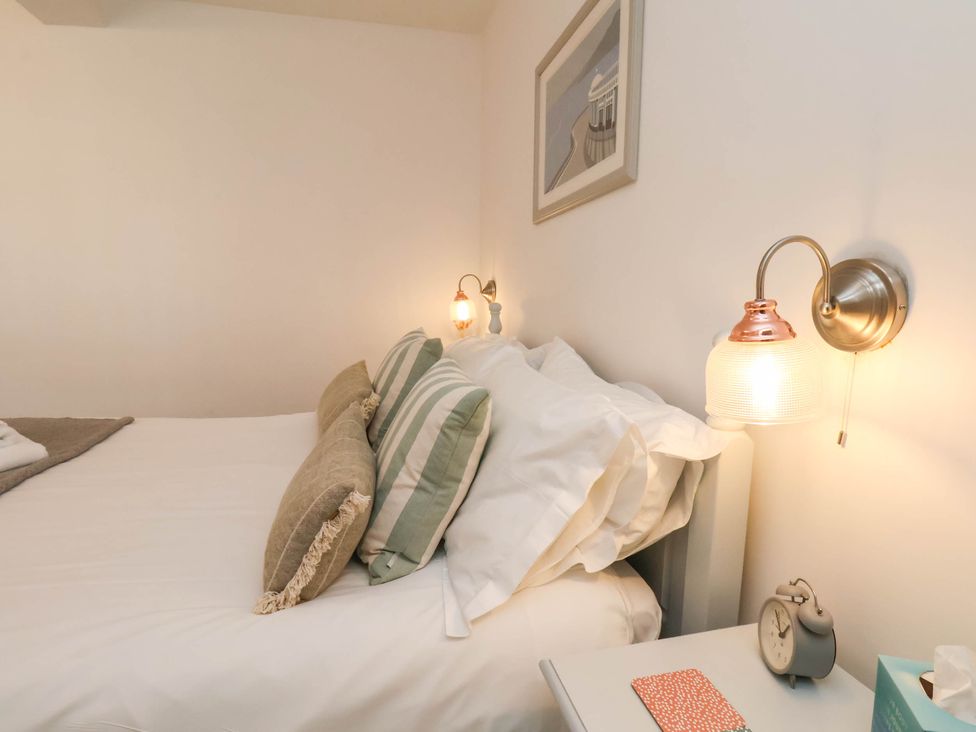 A bedroom with a bed with pillows and a bedside table with a clock and a tissue box at The Riddle in Whitby