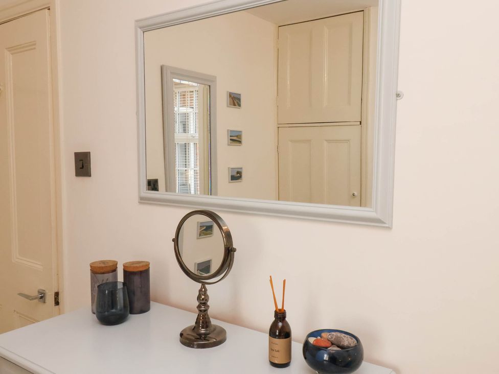 A dresser with jars, a round mirror, an aroma diffuser, and a small bowl in a room with a mirror on the wall at The Riddle in Whitby