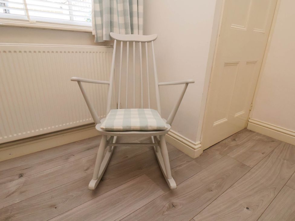 A white rocking chair with a checkered cushion on wooden floor near a radiator and a door