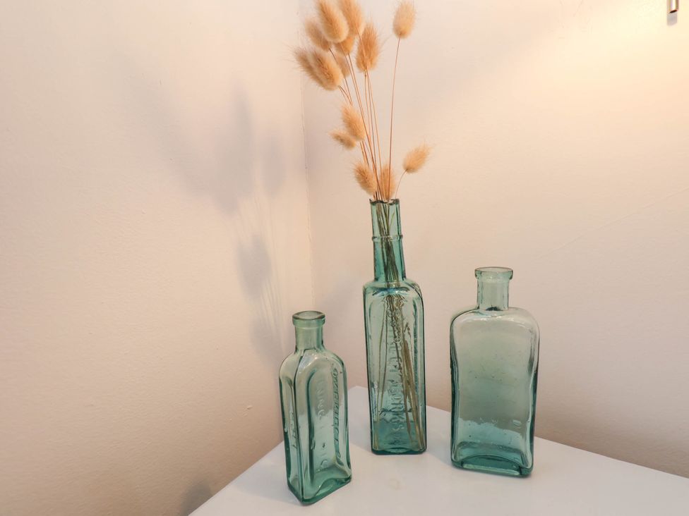 Three green glass bottles on a white surface with dried beige floral stems in one bottle at The Riddle in Whitby