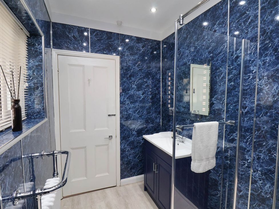 A bathroom with blue marble walls a white door a sink with cabinet a mirror and a glass shower enclosure at The Riddle in Whitby
