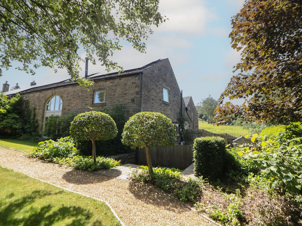 An outdoor view of a house with a garden at Overlea Cowshed in Hayfield