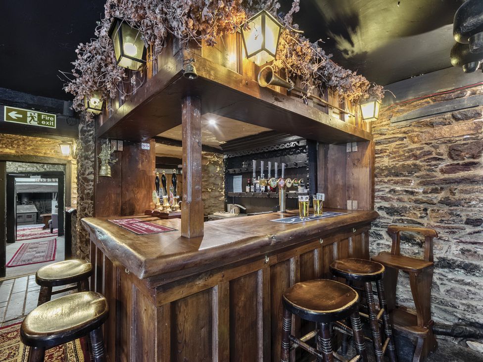 A bar area with wooden counter and stools at The Old Church House in Torbryan
