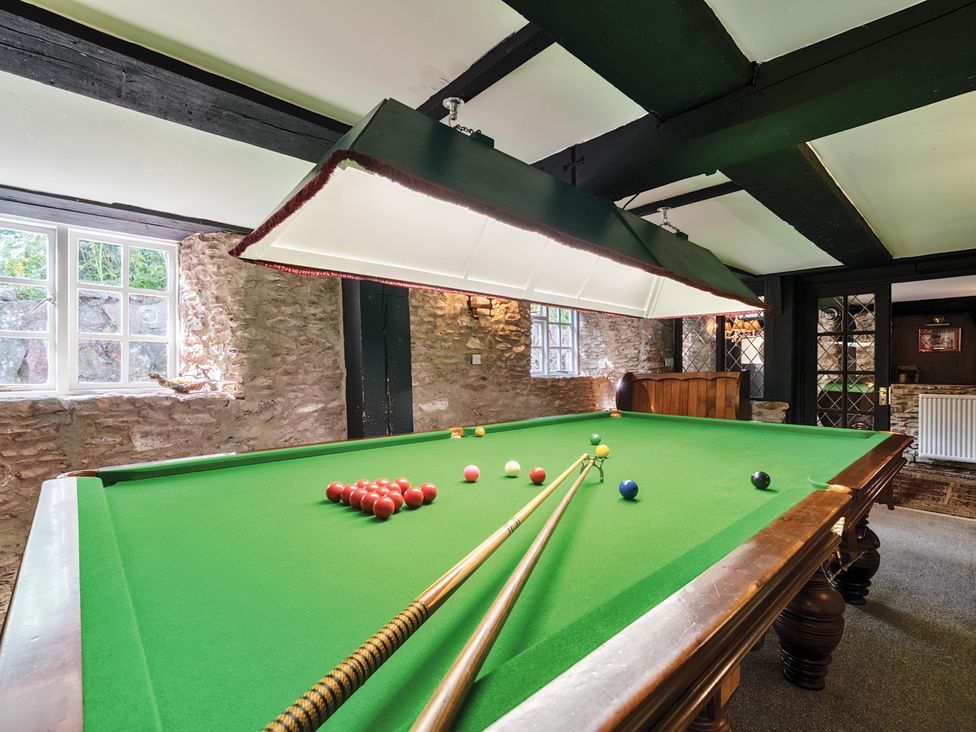 A snooker table with cues in a stone wall room at The Old Church House in Torbryan