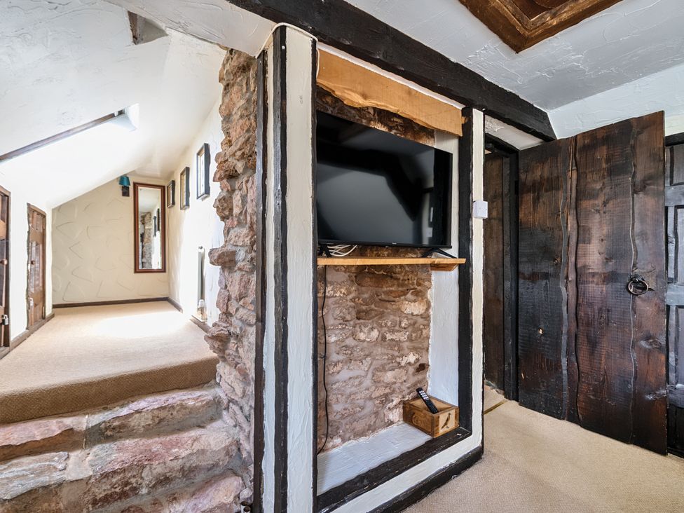 A hallway with a television and stone wall at The Old Church House in Torbryan