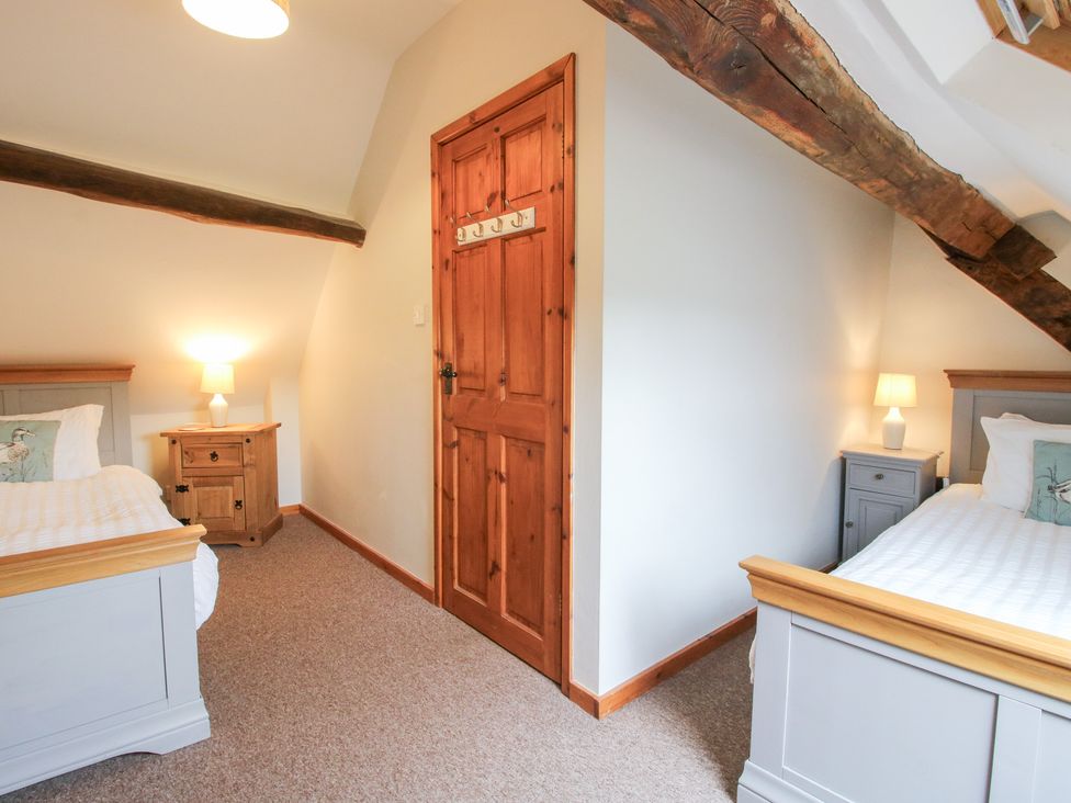 A bedroom with two single beds and a door at Old Hall Barn 3, Church Stretton