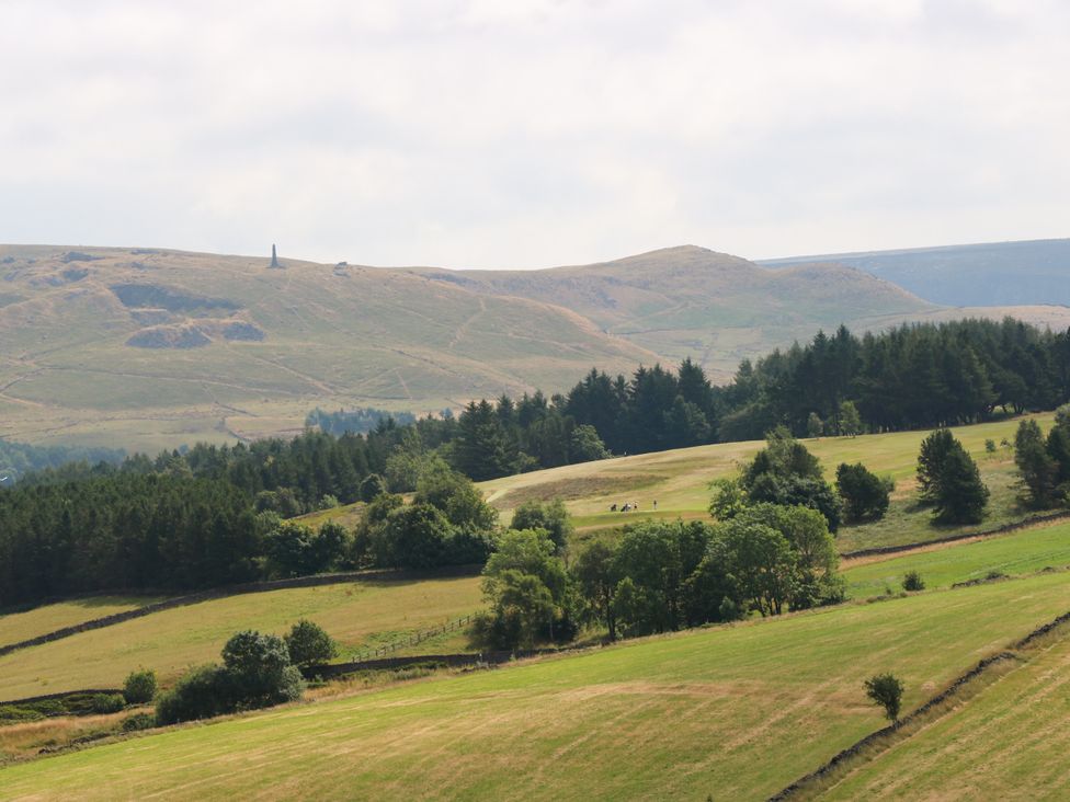 A landscape view showcasing hills, trees, and a stone monument at Upper House Barn in Delph