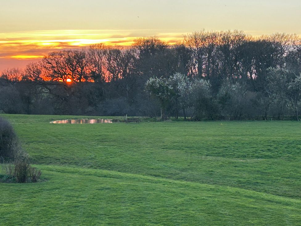 A sunset over grass and trees with a pond at Keepers Cottage in West Knoyle
