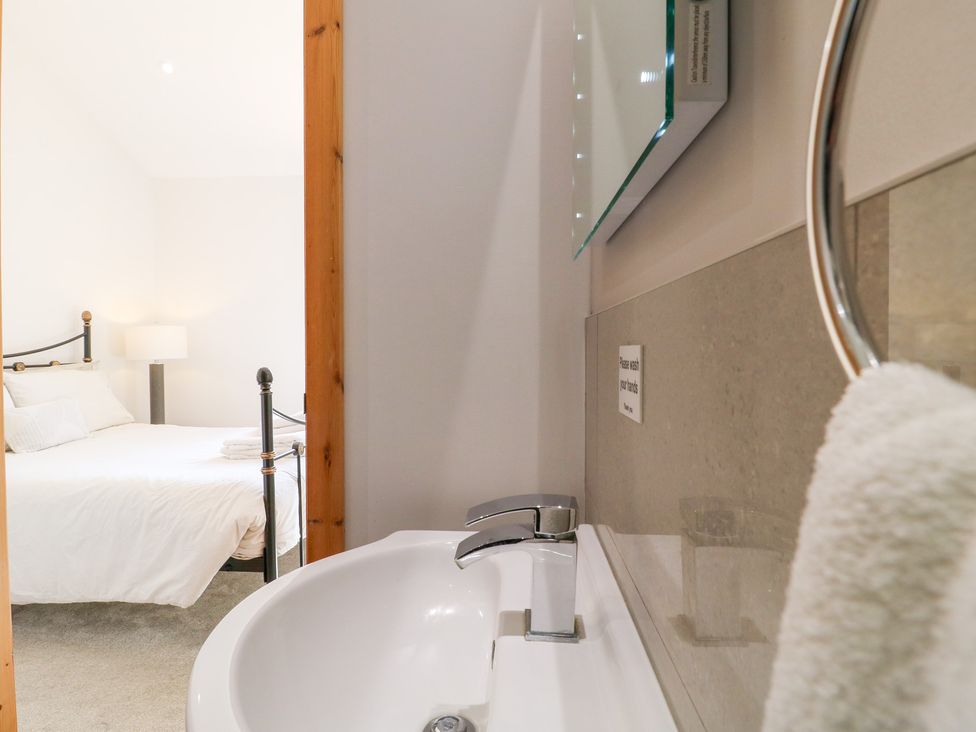 A bathroom with a sink and mirror looking into a bedroom at Mandarin Cottage in Melton Mowbray
