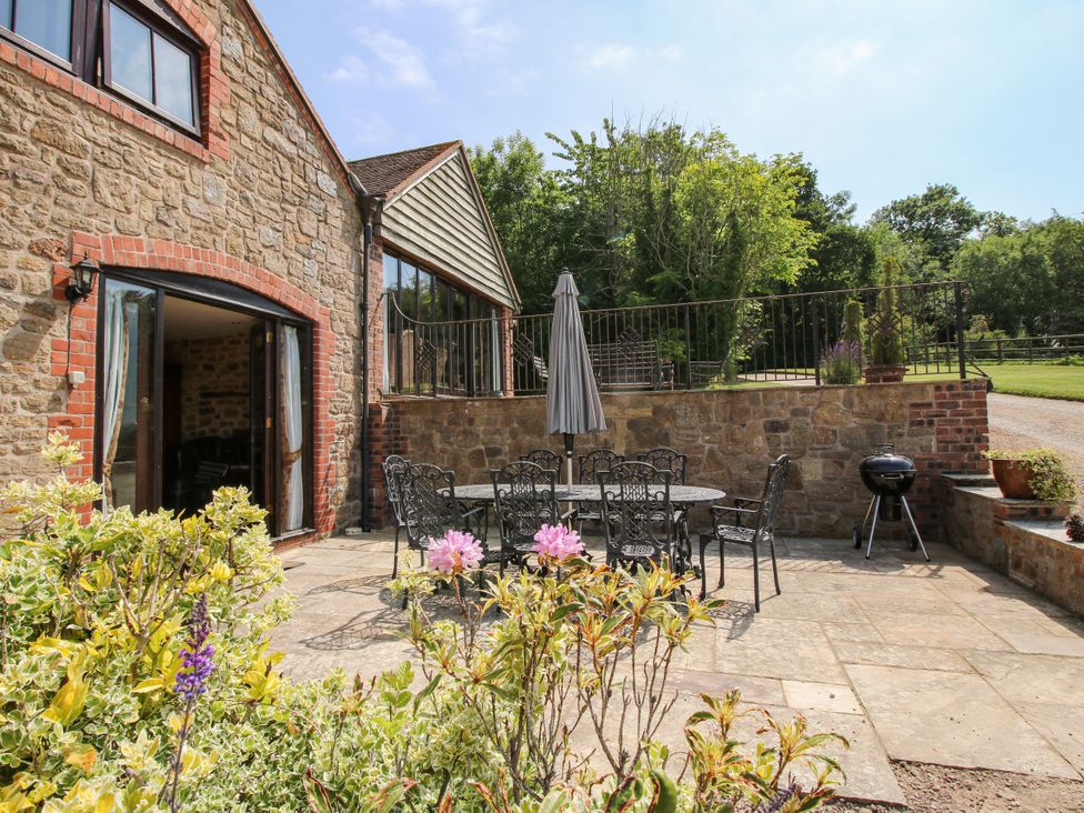 An outdoor patio with a stone wall and a table with chairs at Corn House in Cardington