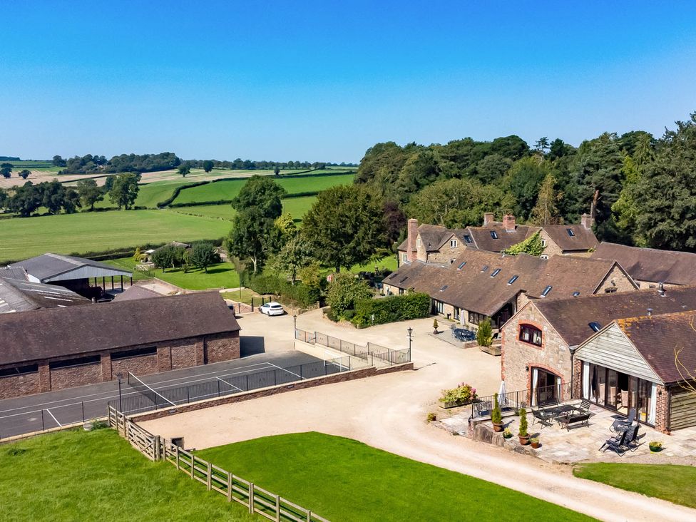 An outdoor view of a house and barn with a tennis court at Corn House in Cardington