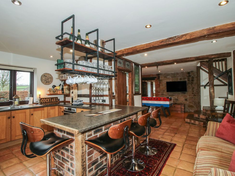 A kitchen with bar stools and shelves at Corn House in Cardington