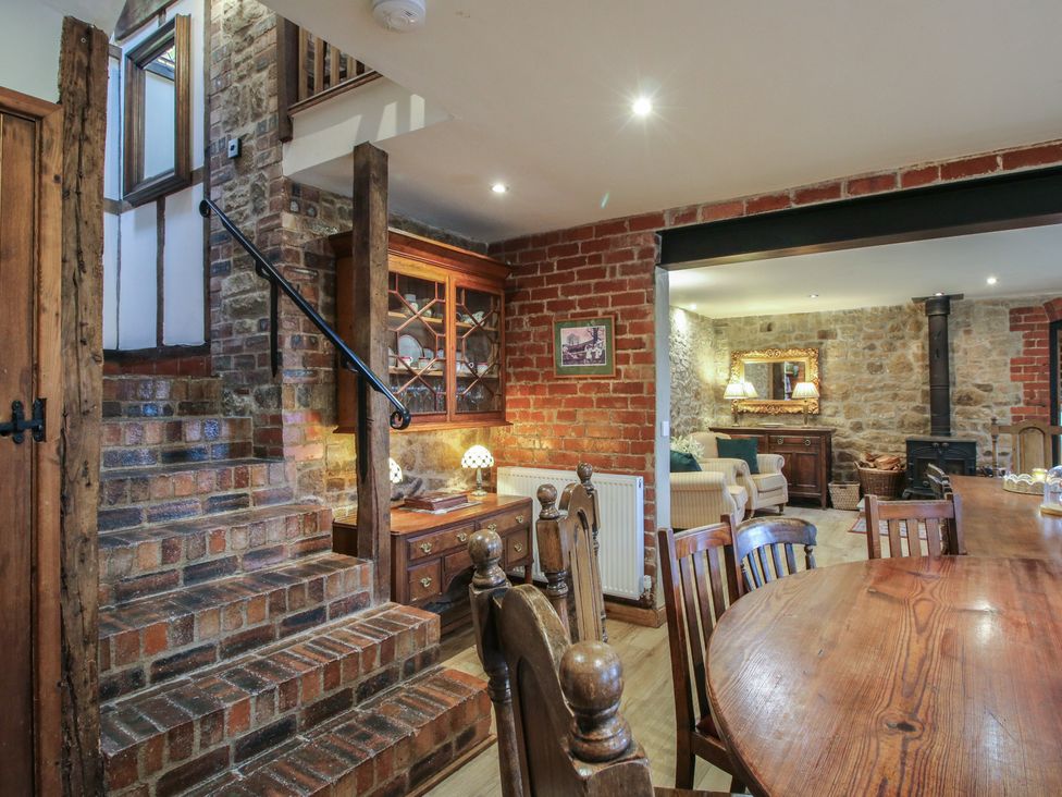 A dining room with a staircase and a display cabinet at Corn House in Cardington