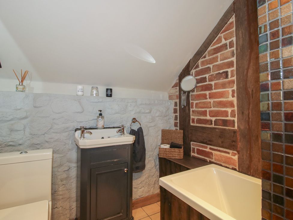A bathroom with a sink, toilet, bathtub, and brick wall at Corn House in Cardington