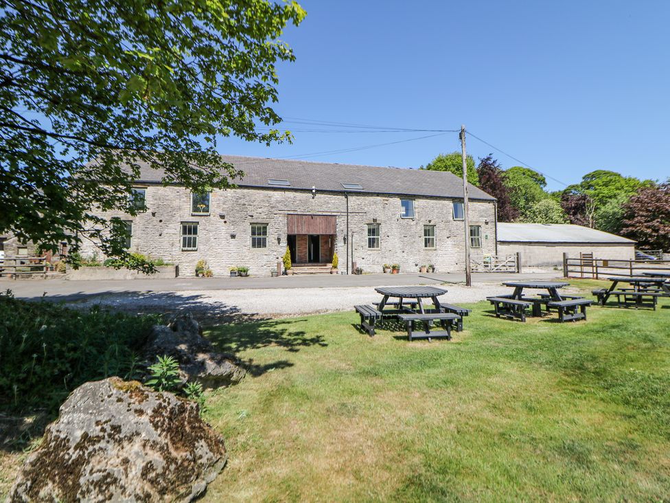 An outdoor area with picnic tables on grass and a stone building with windows and a wooden entrance at Woodlands in Cowdale near Buxton