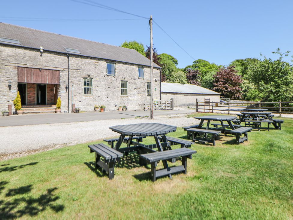 A stone building with wooden picnic tables on grass outside at Woodlands in Cowdale near Buxton