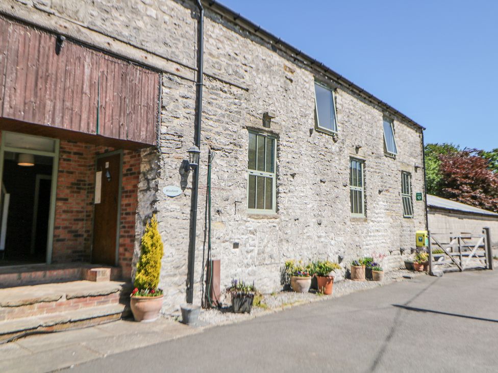 Stone building exterior with potted plants by the windows and a wooden door at Woodlands in Cowdale near Buxton