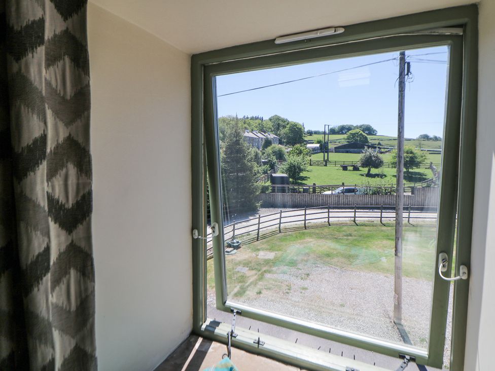 A window open to a view of a green field with trees houses and a utility pole at Woodlands in Cowdale near Buxton