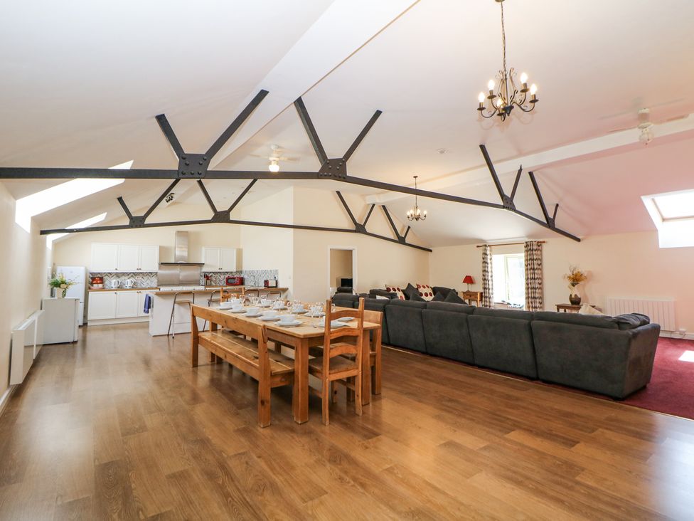An open plan kitchen dining and living area with wooden flooring a wooden dining table set with crockery grey sofas and ceiling beams at Woodlands in Cowdale near Buxton