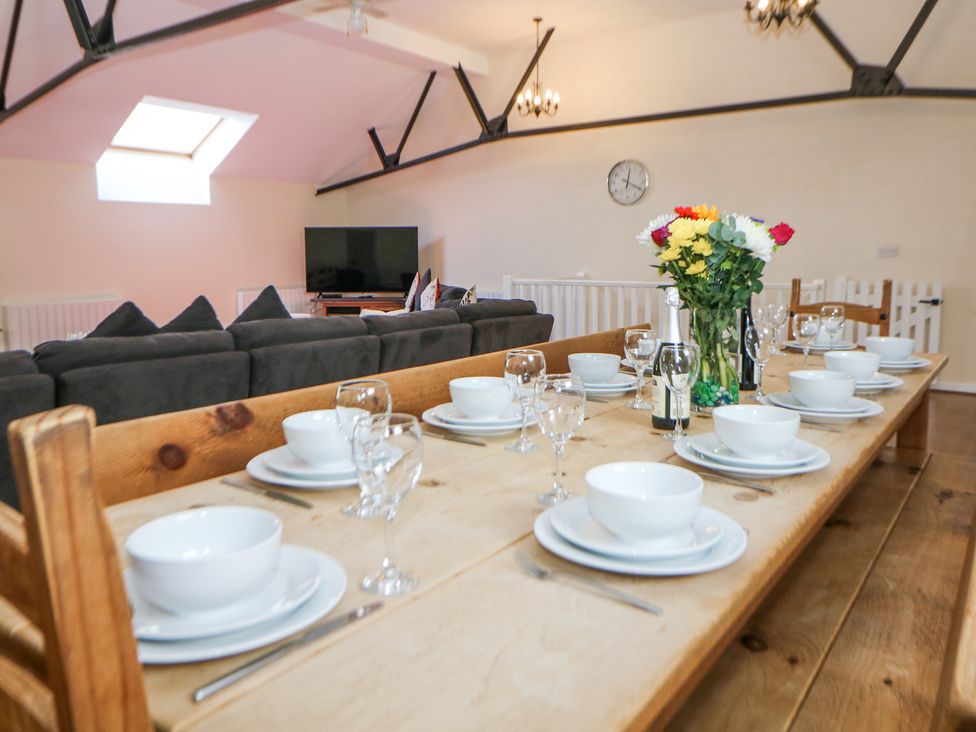 A dining table set with bowls plates glasses and cutlery with a vase of flowers and bottles in a room with a sofa and television at Woodlands in Cowdale near Buxton