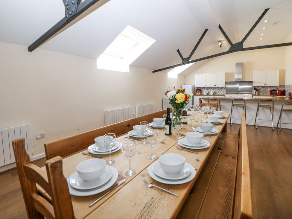 A dining table set with white dishes glasses and cutlery in a kitchen with wooden floor and skylight windows at Woodlands in Cowdale near Buxton