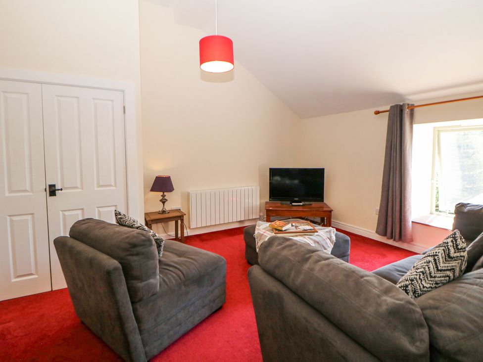 A living room with grey sofas a red carpet a wooden table with a lamp a television and a window with curtains at Woodlands in Cowdale near Buxton