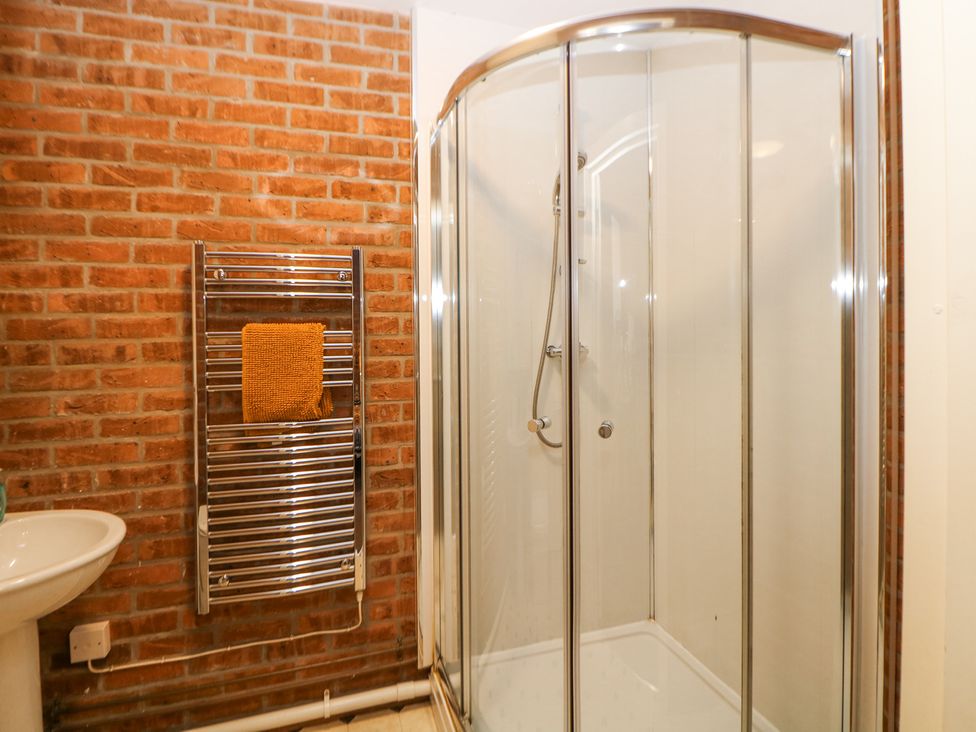A bathroom with a glass shower enclosure a towel rack with an orange towel and a white sink on a brick wall at Woodlands in Cowdale near Buxton
